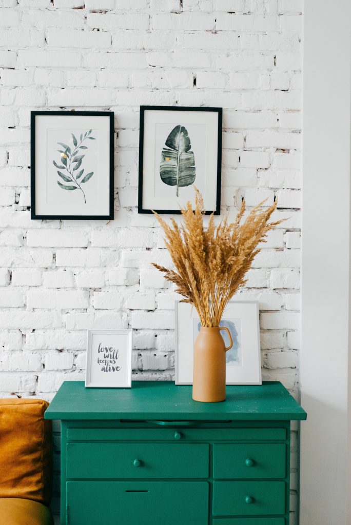 Une commode verte devant un mur de brique et des tableaux